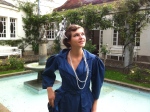 blaues Jugendstilkleid vor Brunnen mit Kopfschmucke und Perlenkette